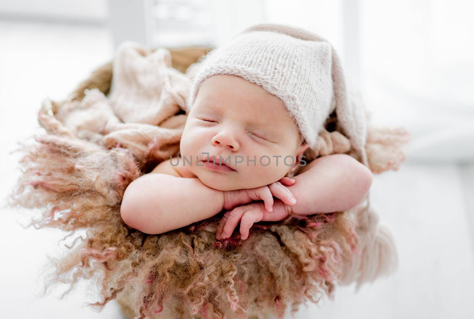 Newborn baby child wearing hat sleeping and holding hands under cheeks. Sweet infant kid napping closeup portrait
