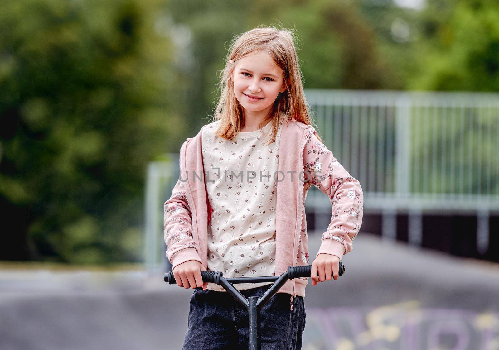 Preteen girl with scooter in city park at spring time portrait. Pretty child kid model posing with vehicle