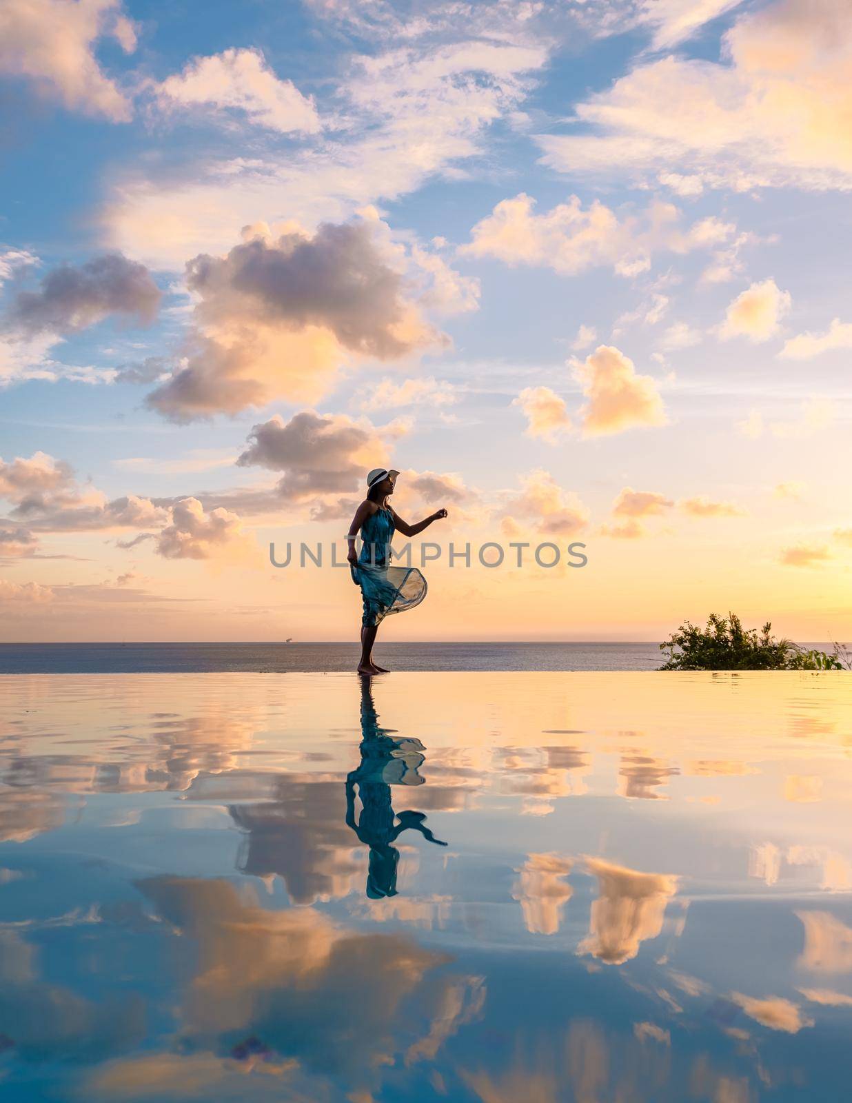 Young women watching the sunset with reflection in the infinity swimming pool at Saint Lucia Caribbean, Asian women at infinity pool during sunset