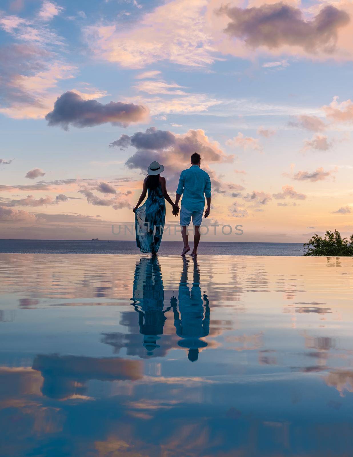 Young men and women watching the sunset with reflection in the infinity swimming pool at Saint Lucia Caribbean, couple at infinity pool during sunset