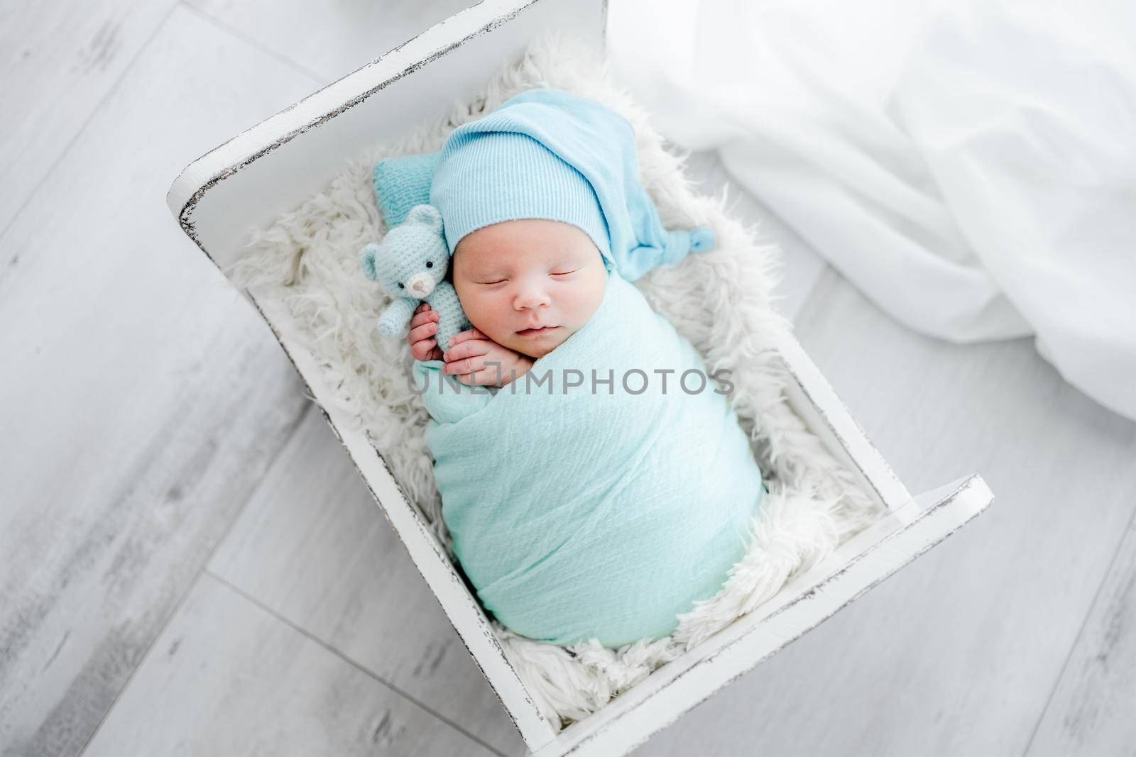 Newborn baby child swaddled in fabric sleeping and holding teddy bear toy. Sweet infant kid napping on fur in tiny bed