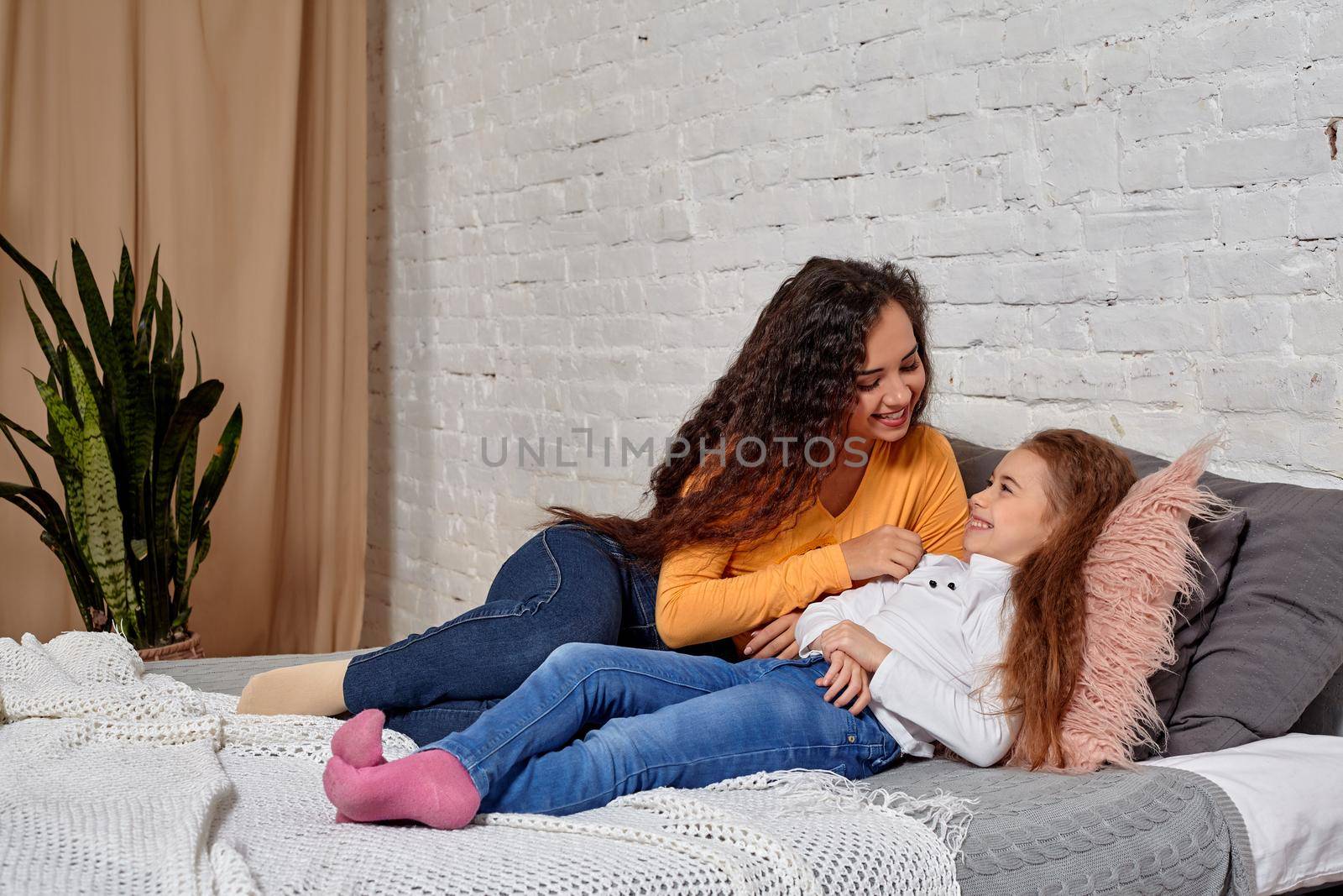 Love of young mother and daughter. They lie on the bed at home and have fun, they feel good.