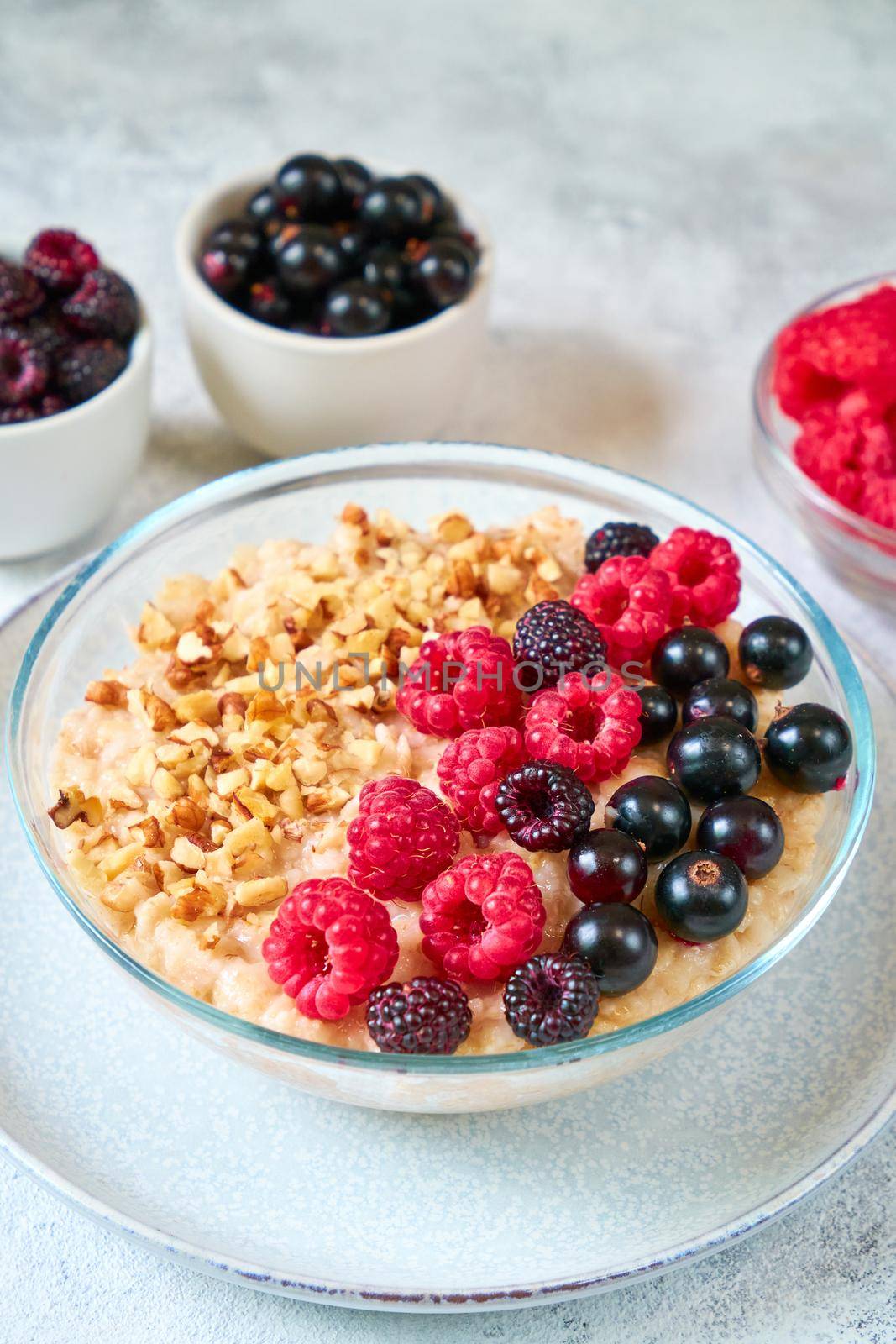 Oatmeal with raspberries, blackcurrants and crushed nuts in a glass bowl. Healthy balanced food by Svetlana_Belozerova