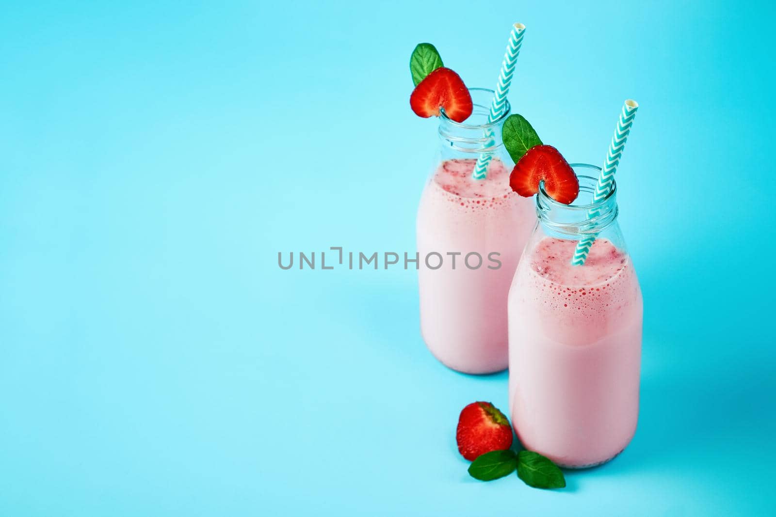 Strawberry smoothie or milkshake in glass jar with berries on blue background. Healthy summer drink.