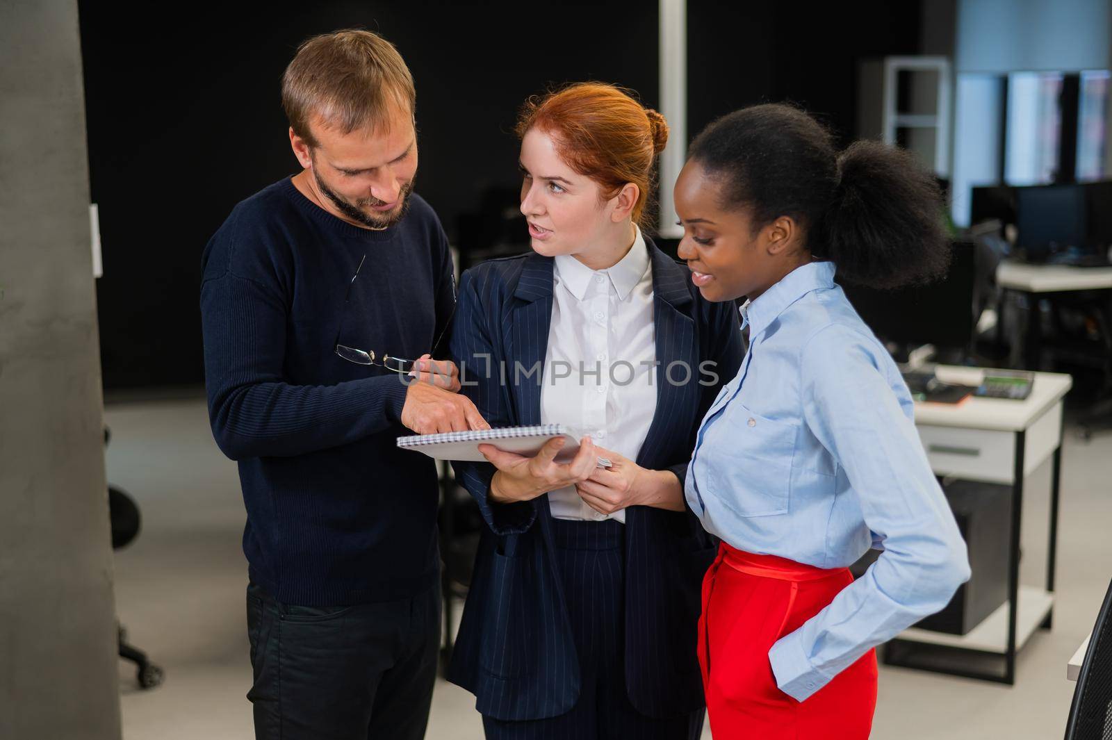 Colleagues discuss work. African young woman, caucasian and red-haired caucasian communicate in the office