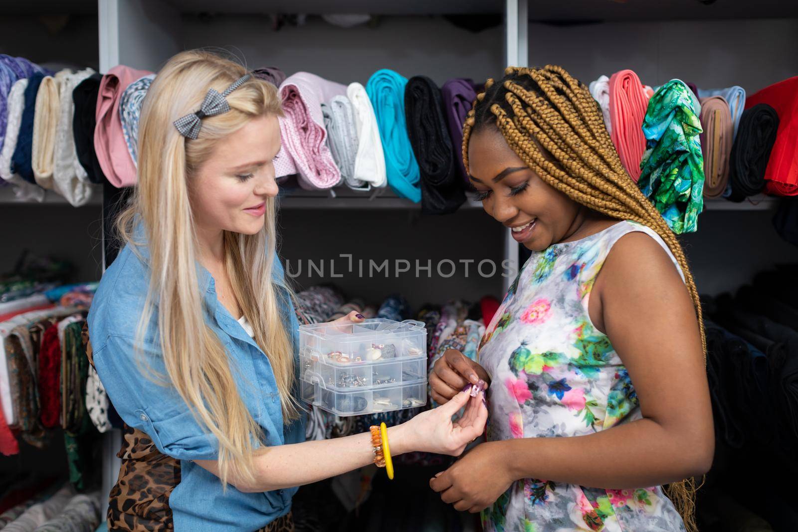 A blonde woman shows small dress accessories to a dark-skinned customer. by fotodrobik
