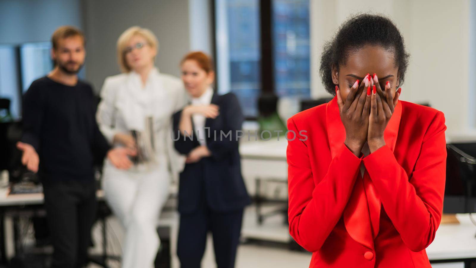 Young african woman crying because of the ridicule of colleagues. Racial discrimination in the office