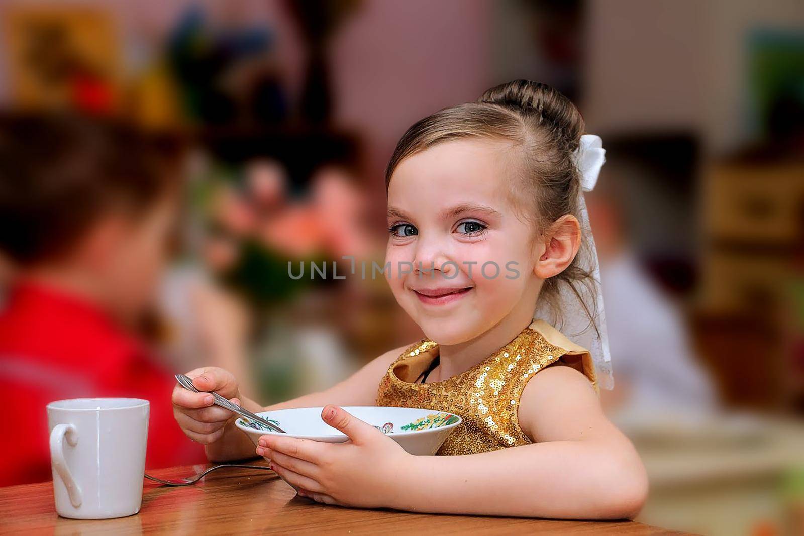 child sits at a table in a cafe. Happy little girl with blonde hair sitting in restaurant. High quality photo