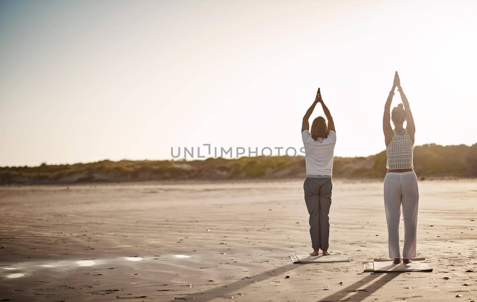 The beach is tranquil, add yoga and it becomes liberating. Rearview shot of an unrecognizable couple practising yoga on the beach
