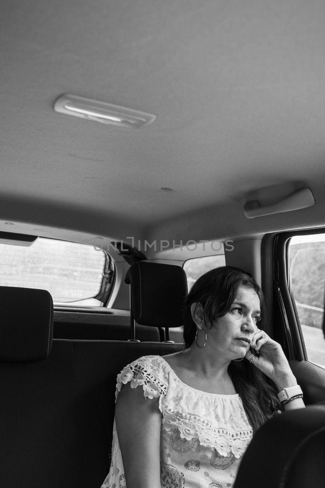 adult hispanic woman in the back seat of a car suv in the mountain road a rainy cloudy day by verbano