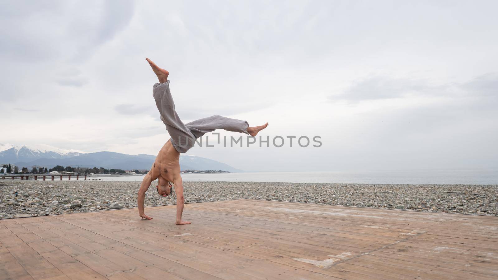 Shirtless caucasian man doing backflip on pebble beach