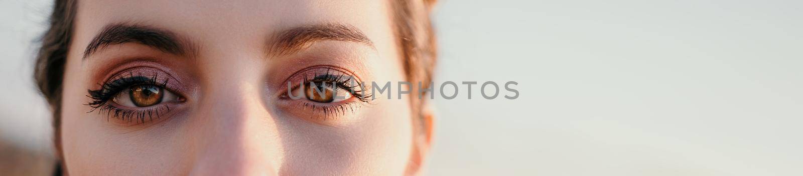Women's eyes banner. Close up portrait of sensual young brunette woman at sunset time and sea background. Cute woman portrait. by panophotograph