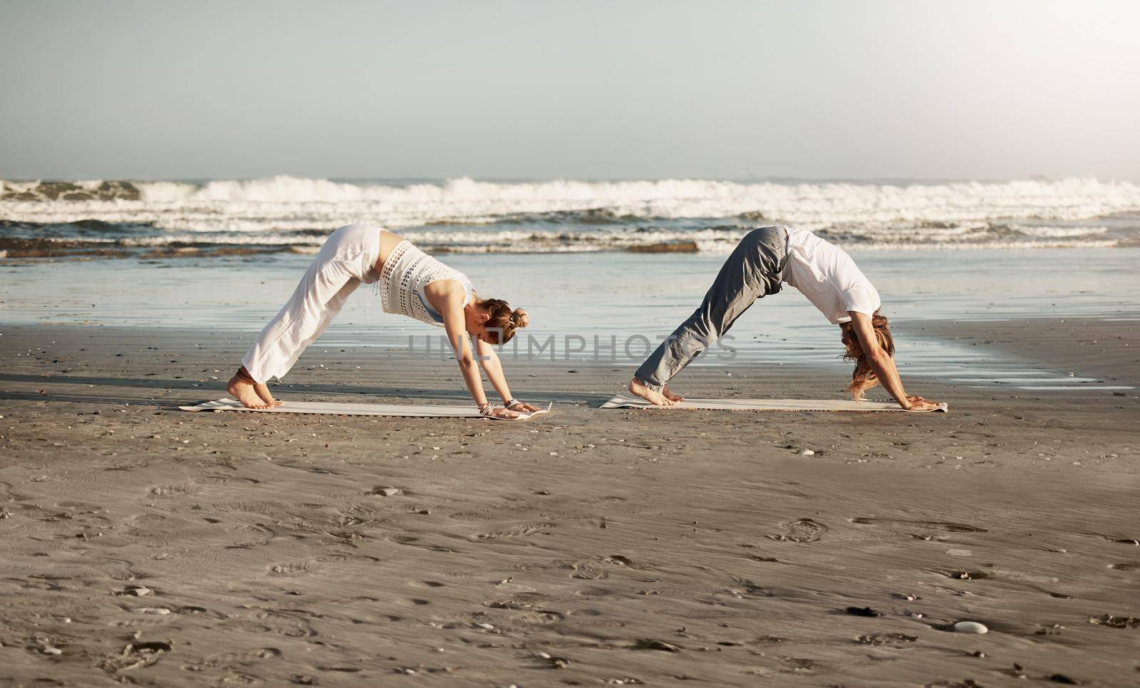 It is through yoga we gain strength and find peace. a young couple practising yoga together on the beach