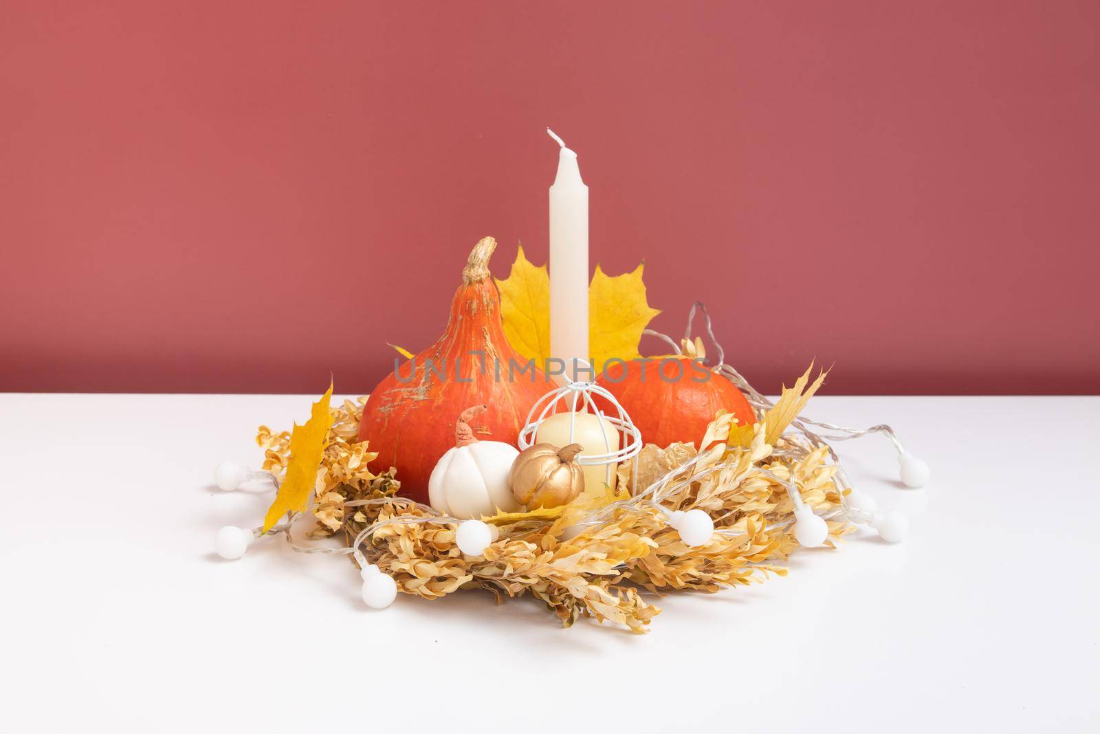Autumn composition. Dried leaves wreath, pumpkins and candle on white pink background. Autumn fall and thanksgiving day concept. Still life.