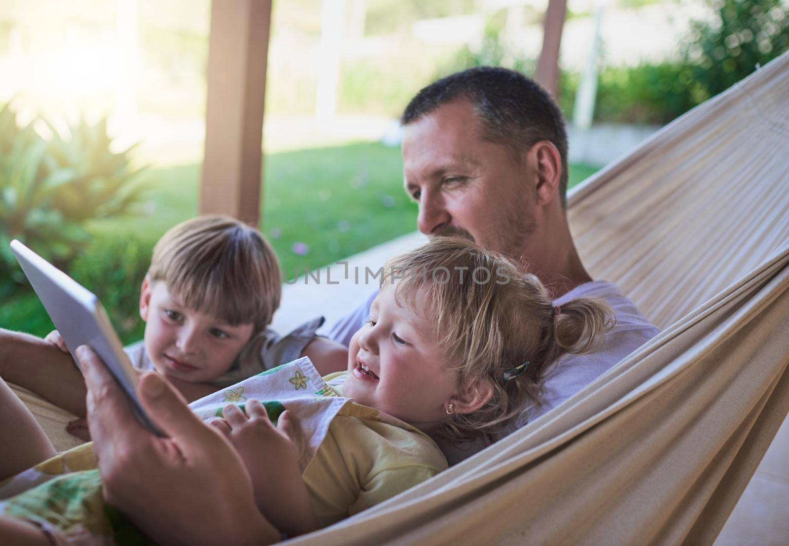 Dads always willing to watch cartoons with his kids. a father and his two little children using a digital tablet while relaxing on a hammock outdoors