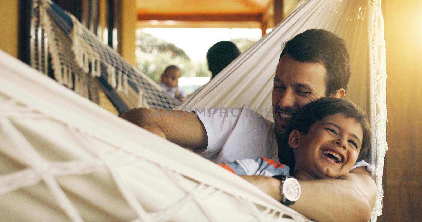 His happiness makes me happy. a father tickling his adorable son on a hammock outside. by YuriArcurs