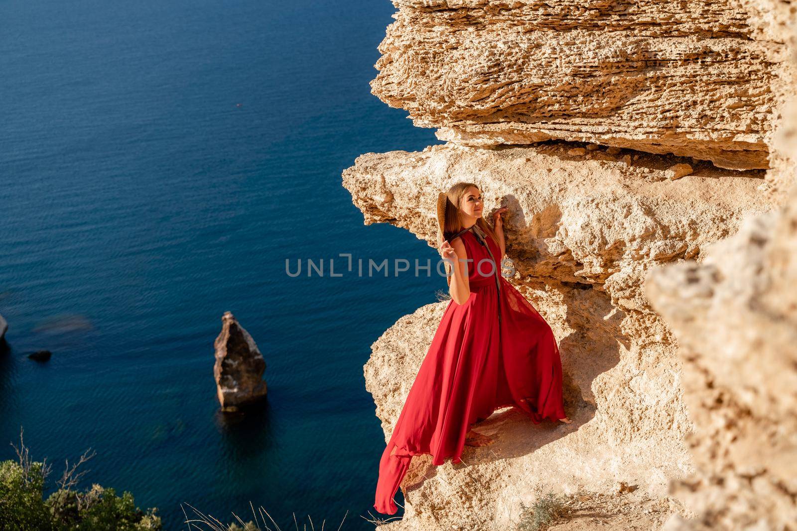 A woman in a red flying dress fluttering in the wind, against the backdrop of the sea