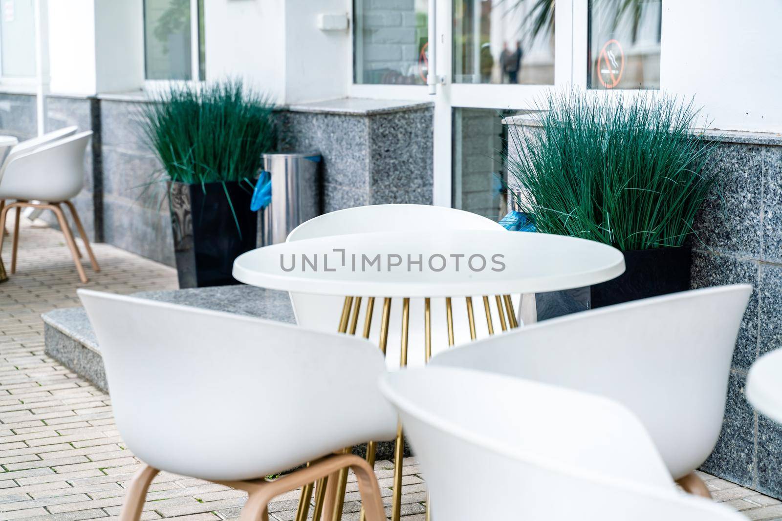 Street cafe with white chairs, green foliage around. Without people, tourism, travel