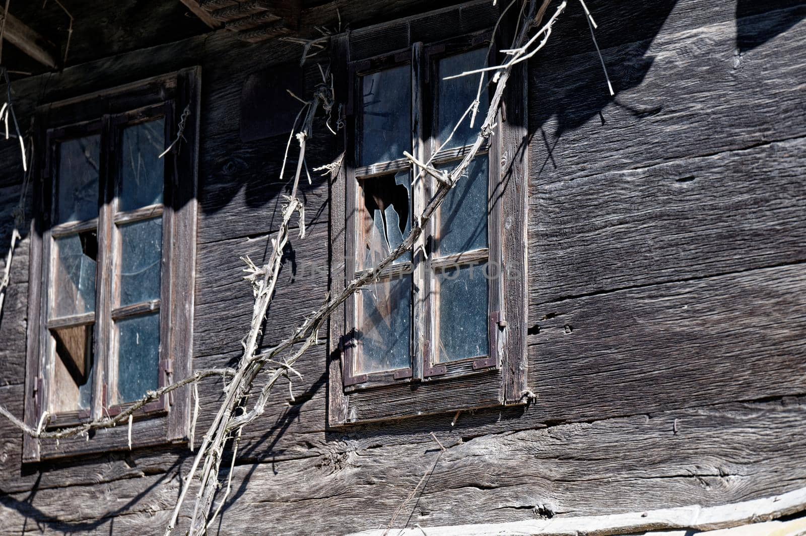 Two windows with broken windows at an old uninhabited wooden house.