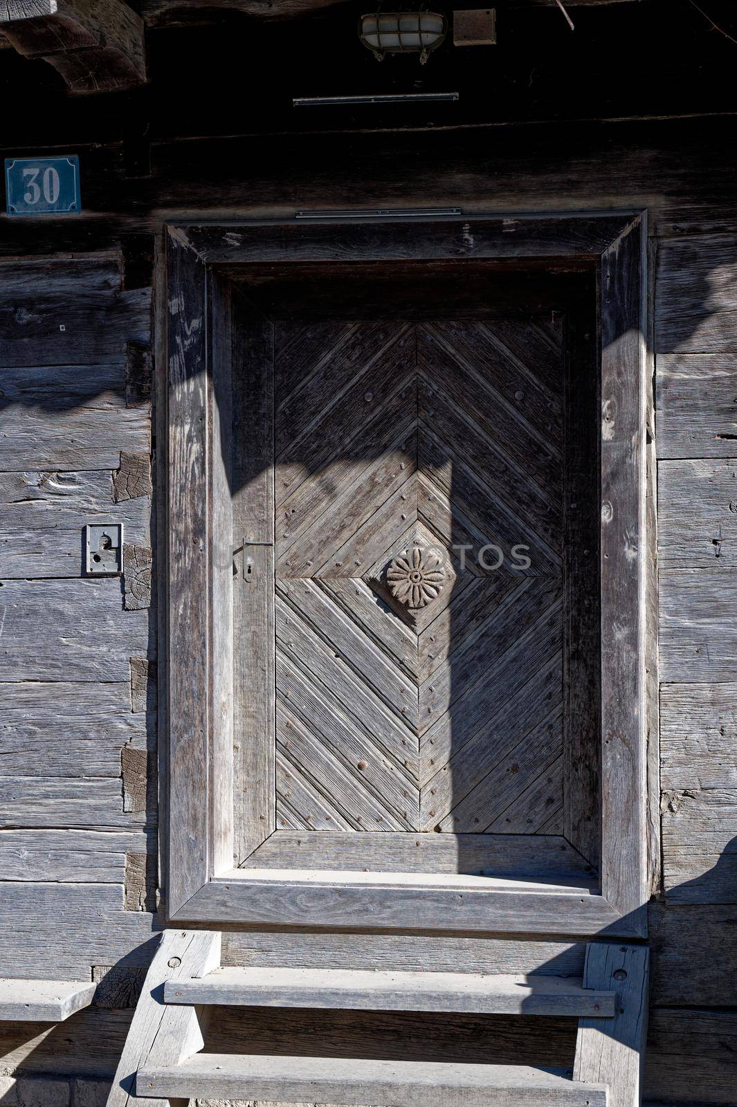 Front door with the number 30 at an old wooden house with a small electric lamp above the door stick.