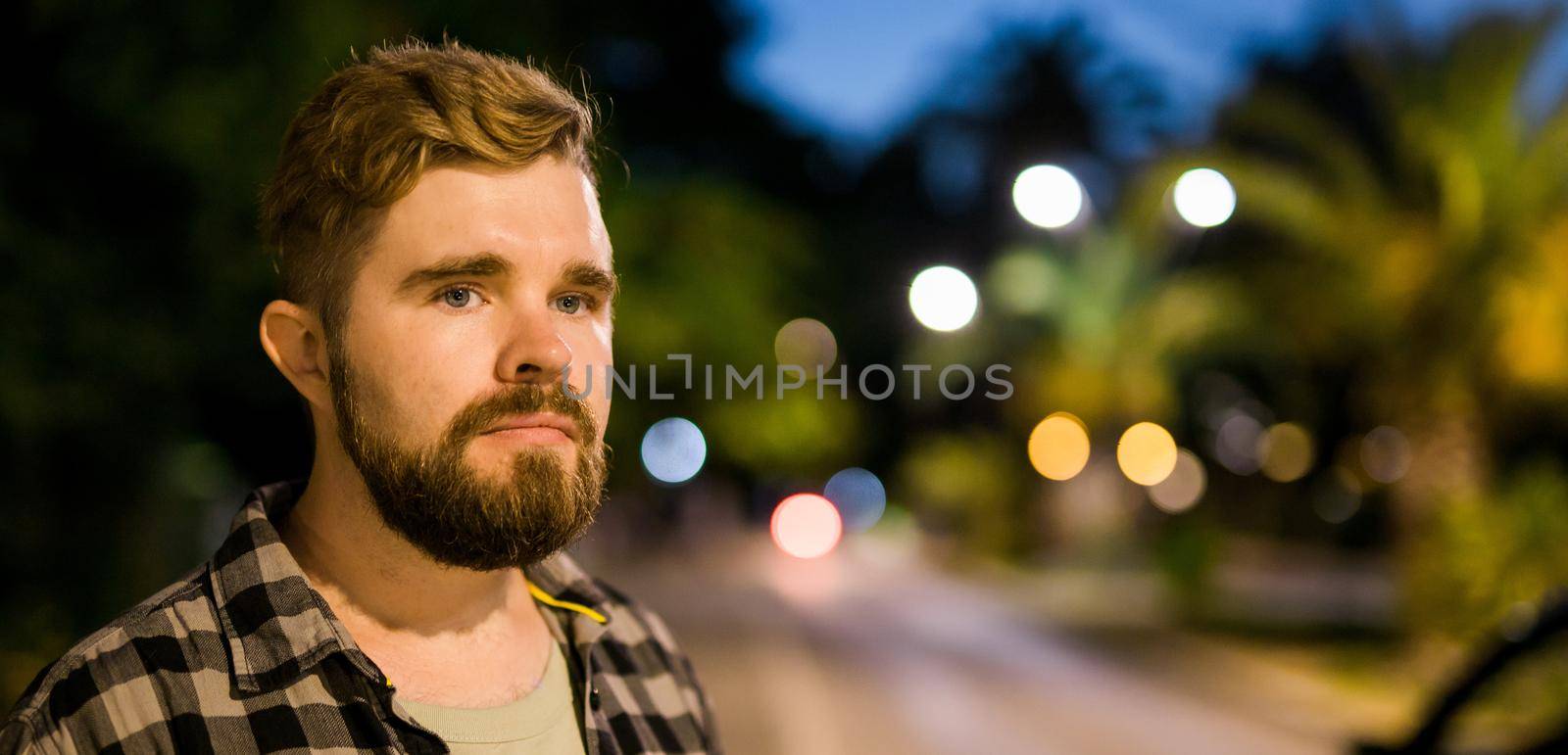 Portrait of man standing in night city street with bokeh street lights background. Confident lonely guy. Close-up portrait