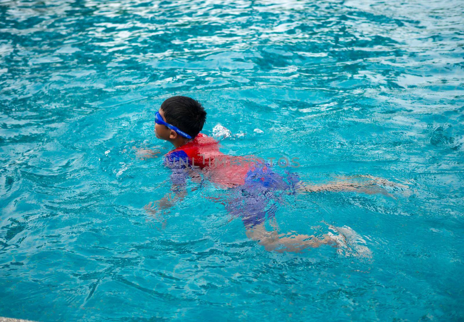 boy wearing a swimsuit and glasses swimming in the middle of the pool with a blue water background by Unimages2527