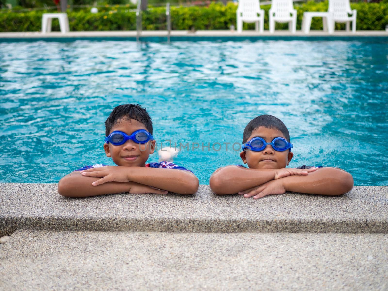 brothers wearing swimsuits and glasses Smile while perched on the edge of the pool. by Unimages2527