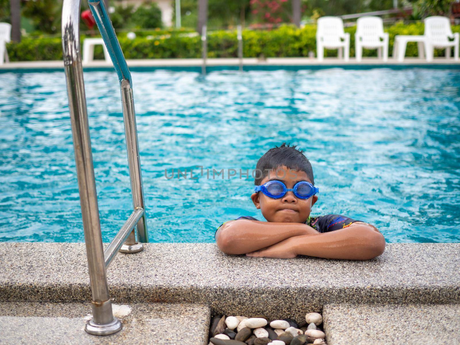 The boy wearing swimsuits and glasses Smile while perched on the edge of the swimming pool. by Unimages2527