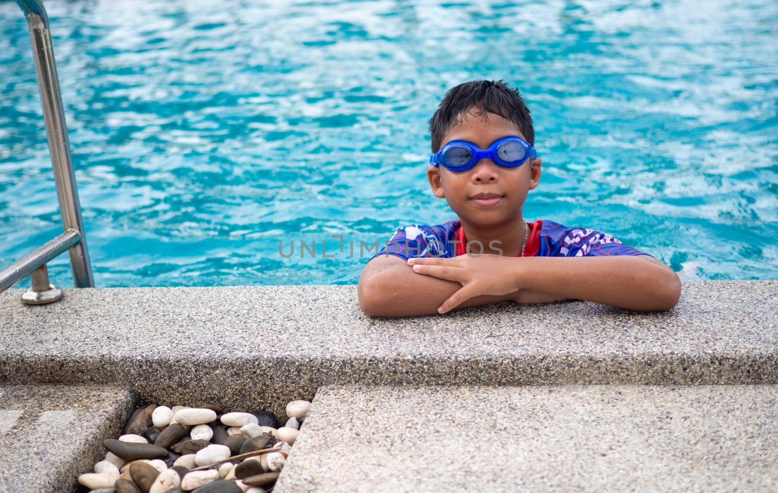 The boy wearing swimsuits and glasses Smile while perched on the edge of the swimming pool. by Unimages2527