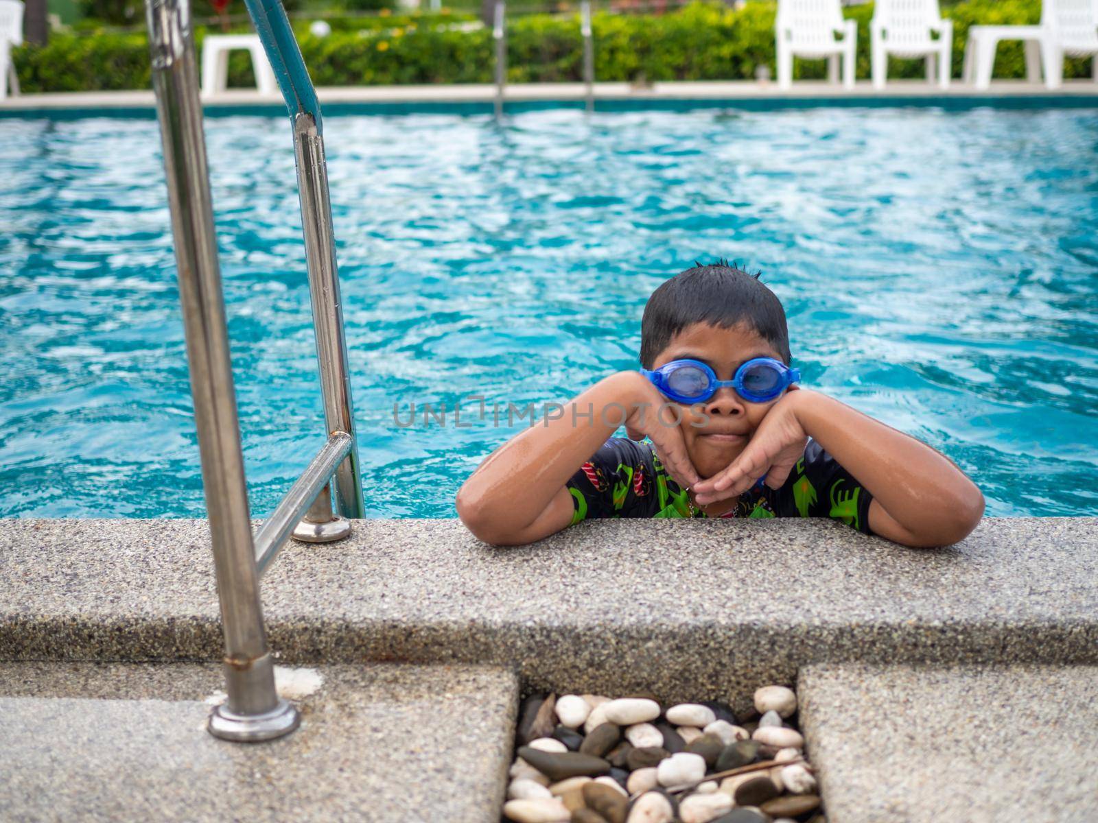 The boy wearing swimsuits and glasses Smile while perched on the edge of the swimming pool. by Unimages2527