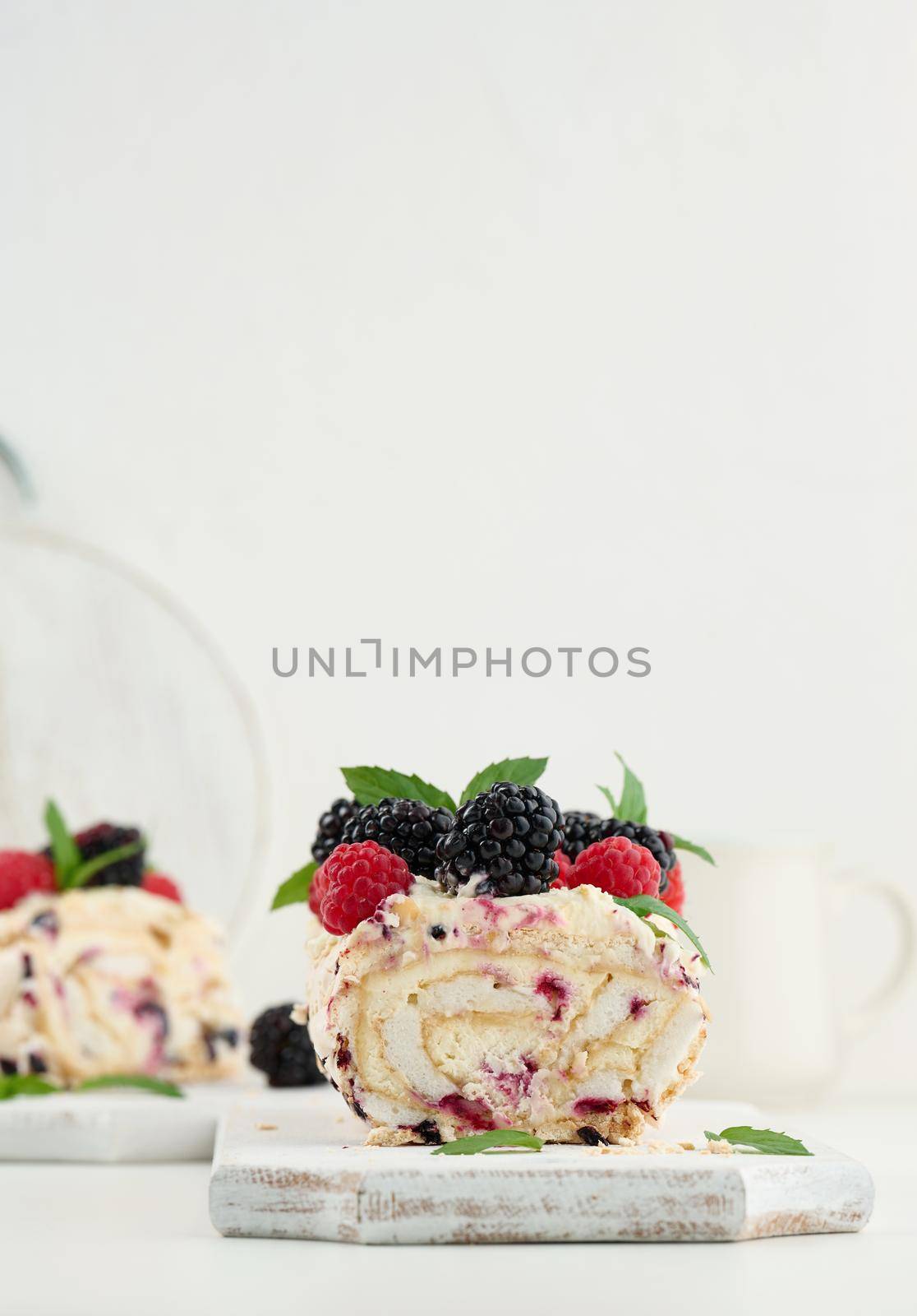 Baked meringue roll with cream and fresh fruits on a white wooden board, delicious dessert