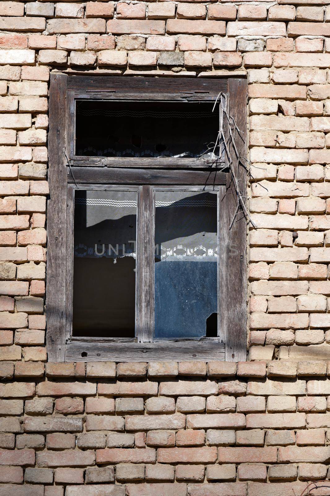 Detail of an old abandoned house with broken window panes, with a brick wall.