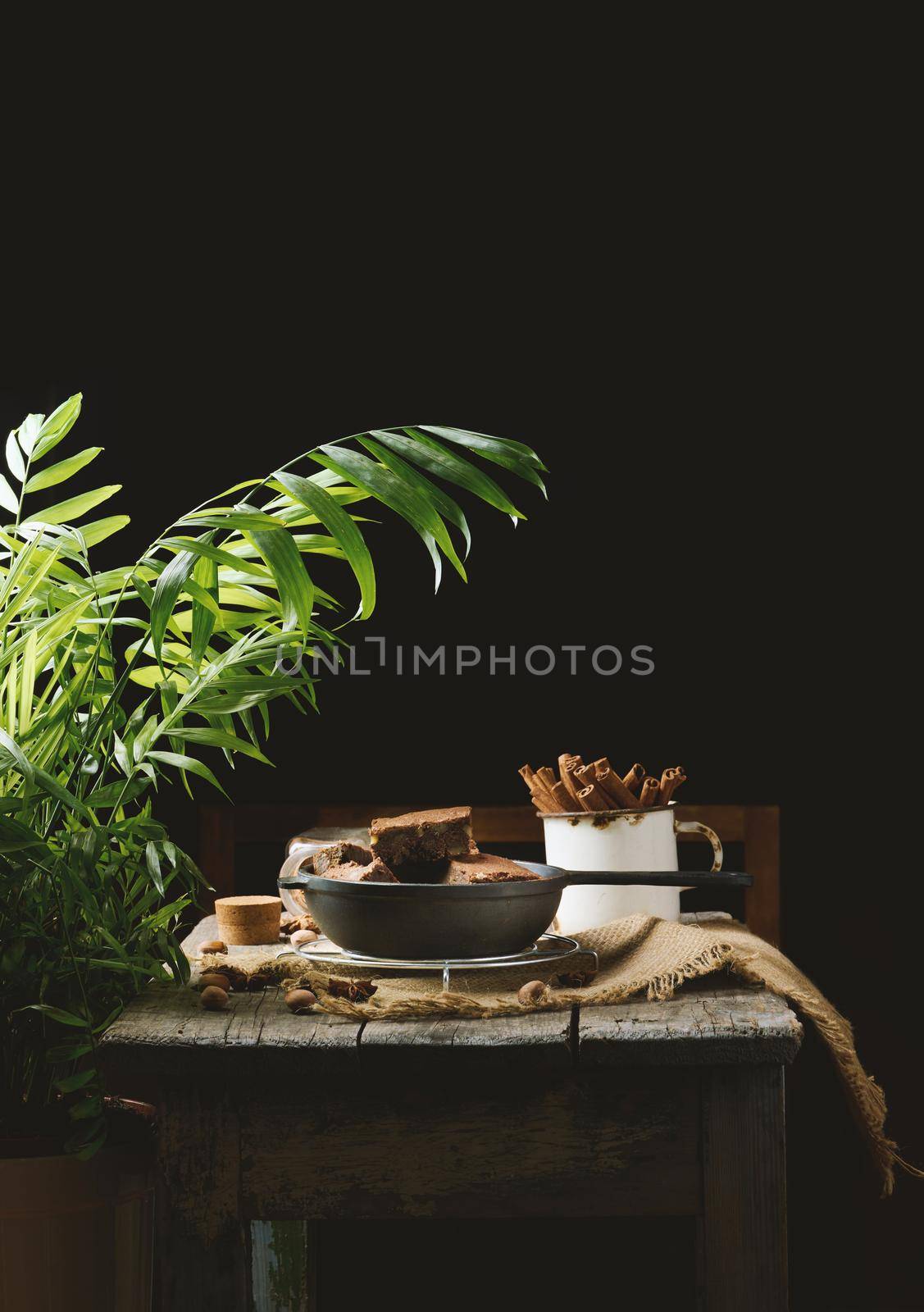 Baked pieces of chocolate brownie cake with walnuts in a black metal frying pan on a wooden table