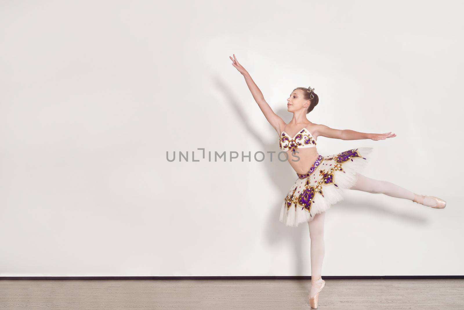 A young ballerina performs ballet exercises in the studio against a white background
