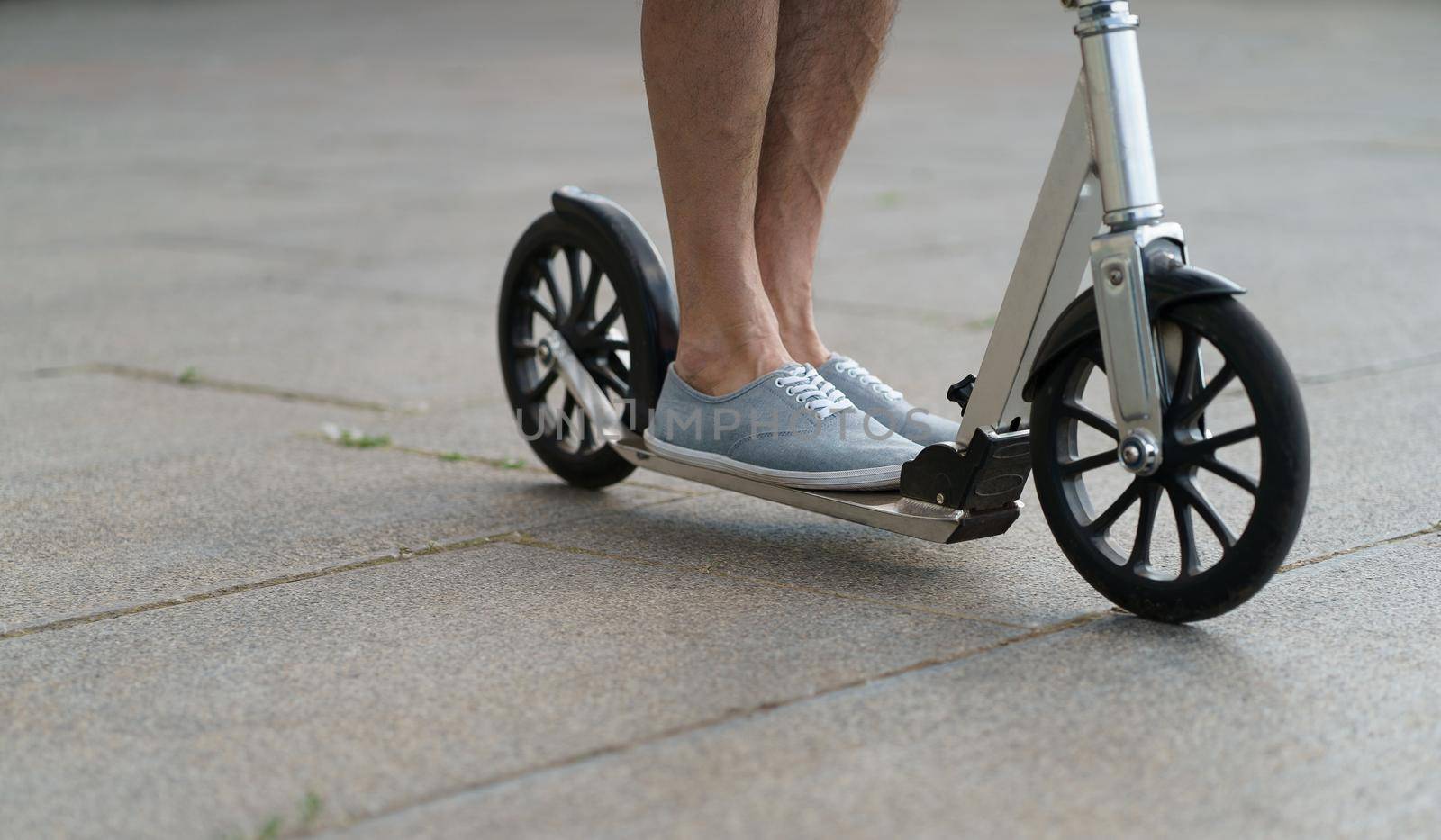 Man feet on scooter close up wearing in a sneakers shoes. Scooter with big wheels man having a ride on the streets or park after work outdoors. No face visible. Selective focus on feet.