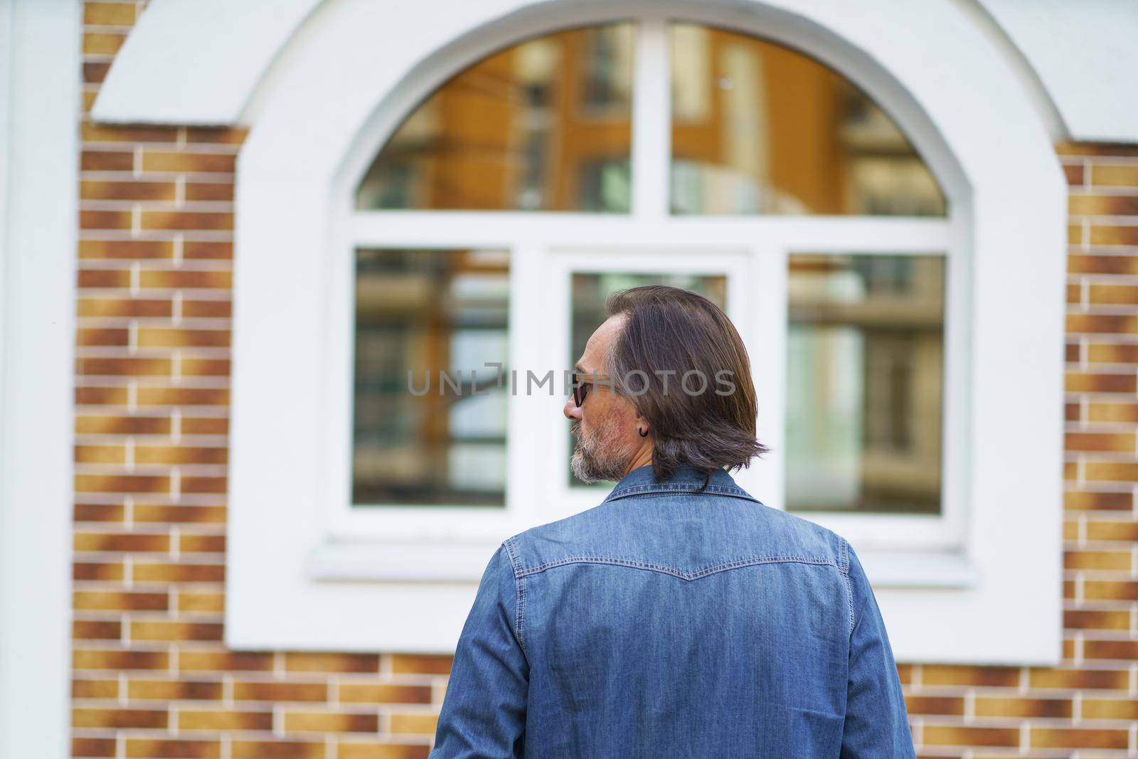 Close up rear view of a man standing alone in front old town building looking sideways while traveling in european cities during vacation time wearing denim jeans shirt. Travel concept.