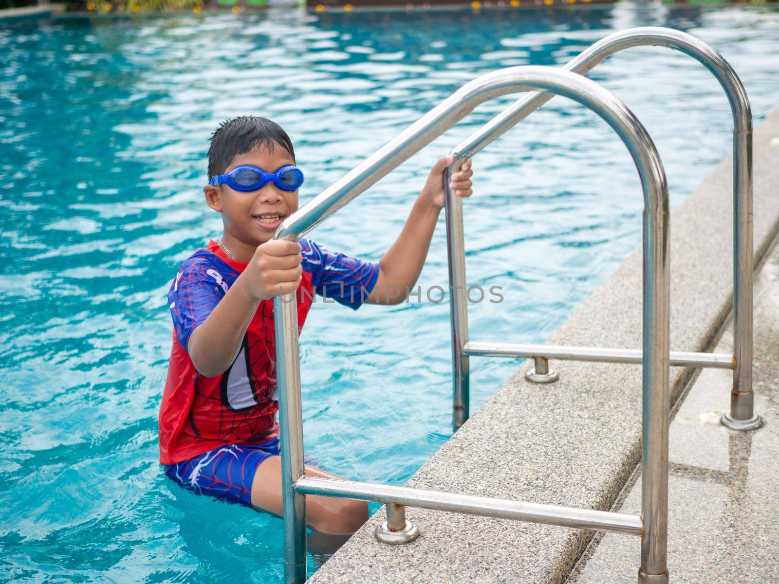 The boy wearing swimming goggles on blue pool ladder red swimsuit