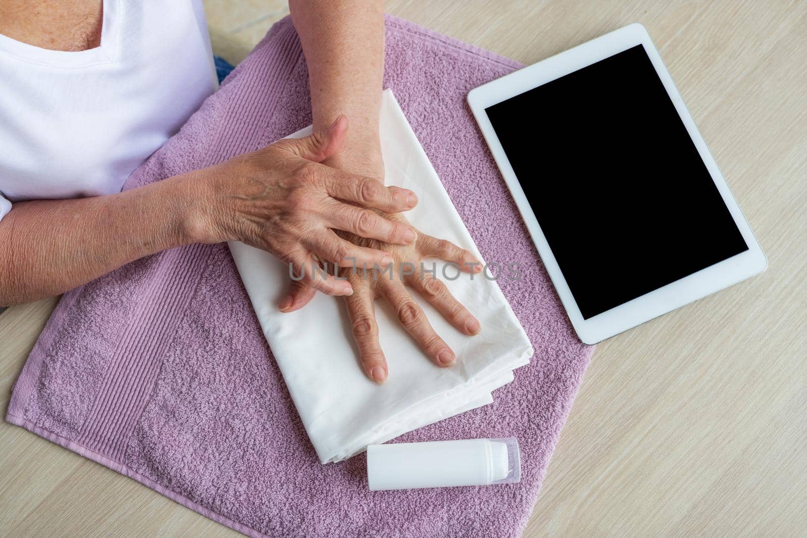 Close-up, top view. An elderly woman looks at a tablet and does self-massage of her hands. Mockup for tablet, mobile application, instructions. Prevention of age-related changes in the elderly