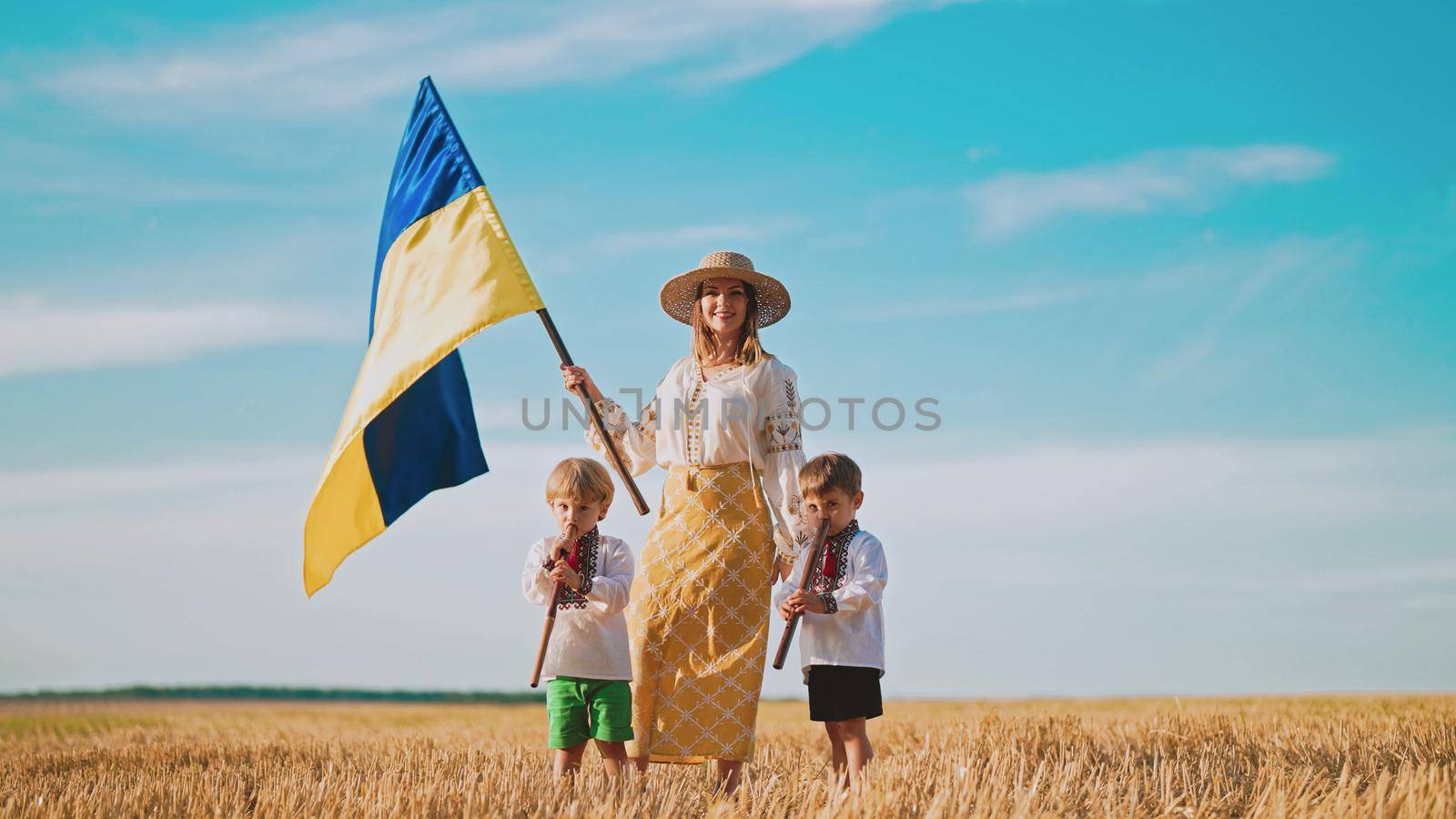 Ukrainian mother with children sons waving national flag in wheat field. Woman in embroidery vyshyvanka. Boys playing flutes. Ukraine, independence, freedom, patriot symbol, VICTORY, win in war. by kristina_kokhanova