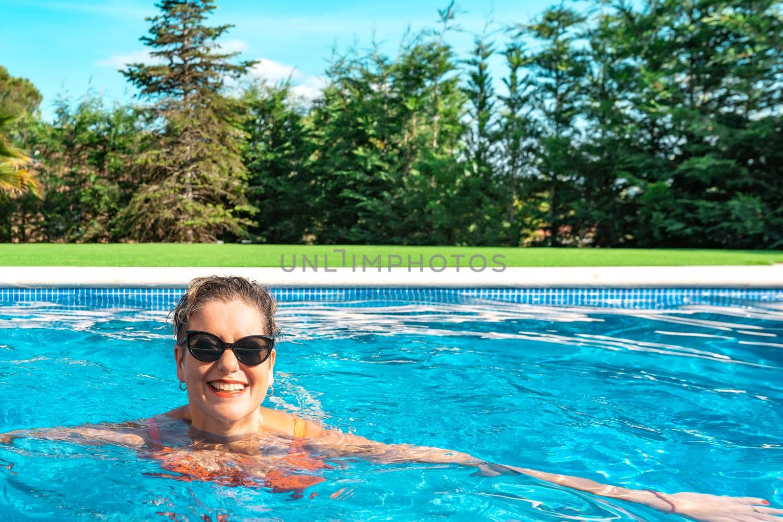 mature woman swimming happily in the pool at home on summer holidays. business woman swimming in her free time. holiday and travel concept. outdoor garden, natural sunlight.