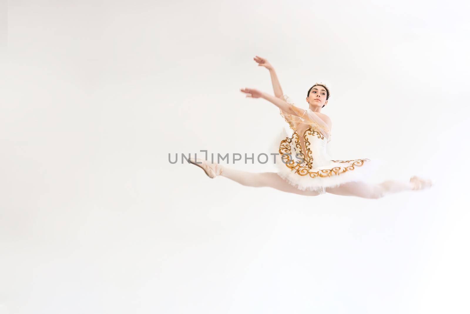 A young charming ballerina does ballet exercises in a jump against a white background