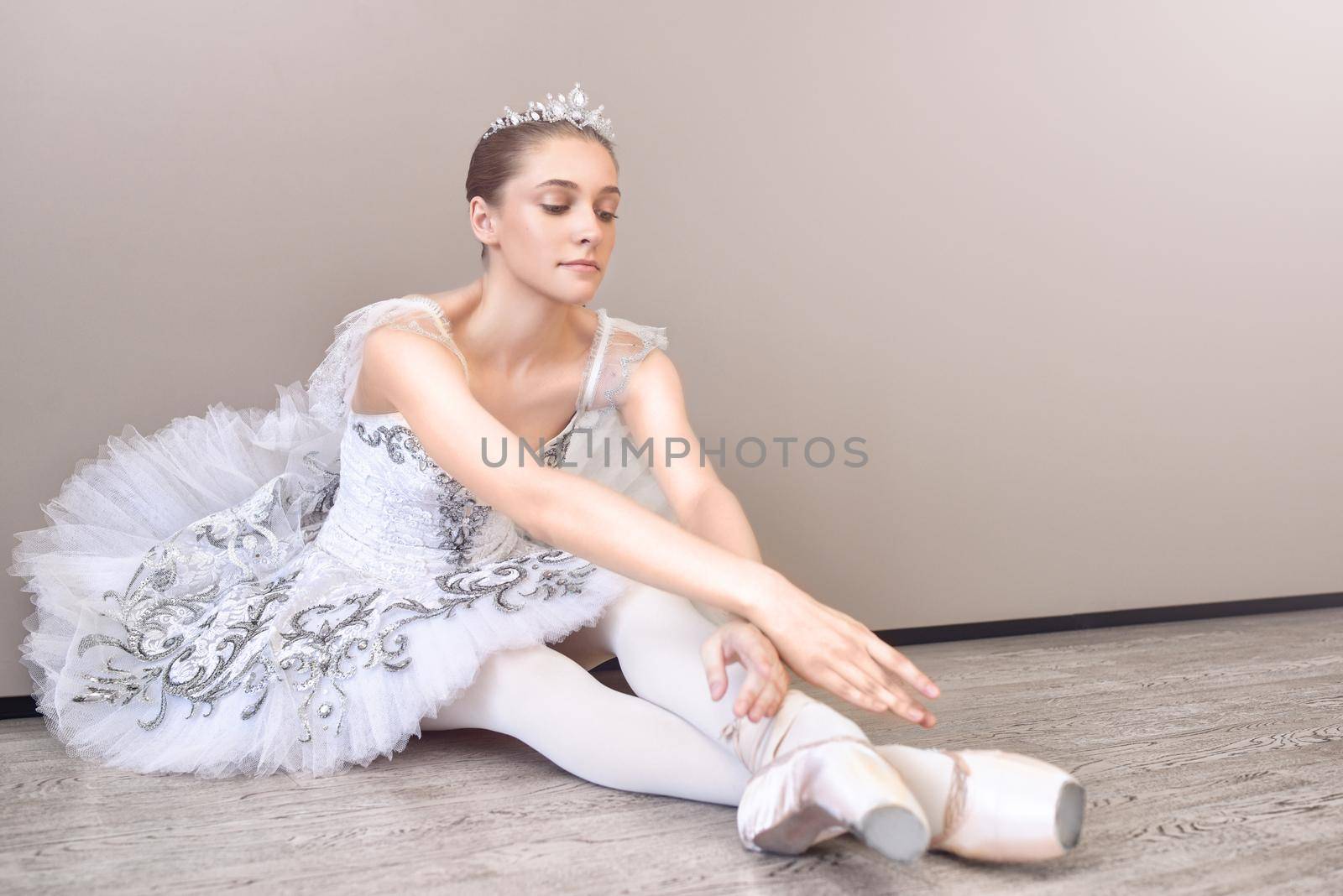 a cute ballerina sitting on the floor with her arms outstretched forward, practicing ballet poses in the studio by Nickstock