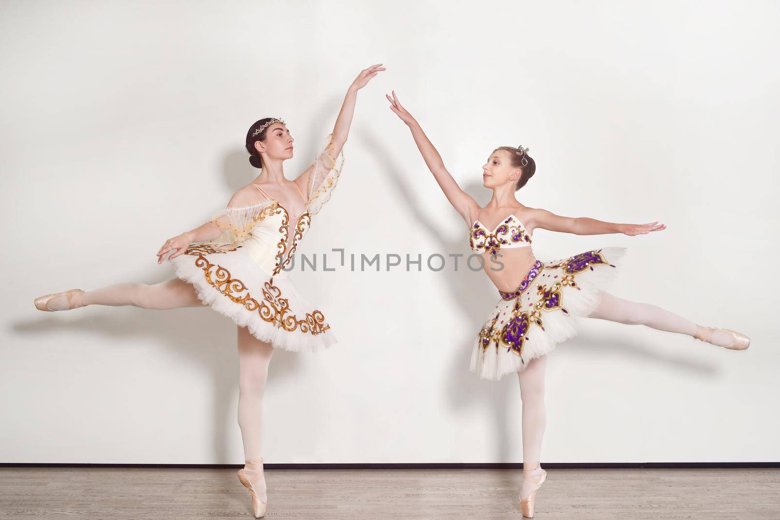Two ballerinas young practicing ballet poses against a white background