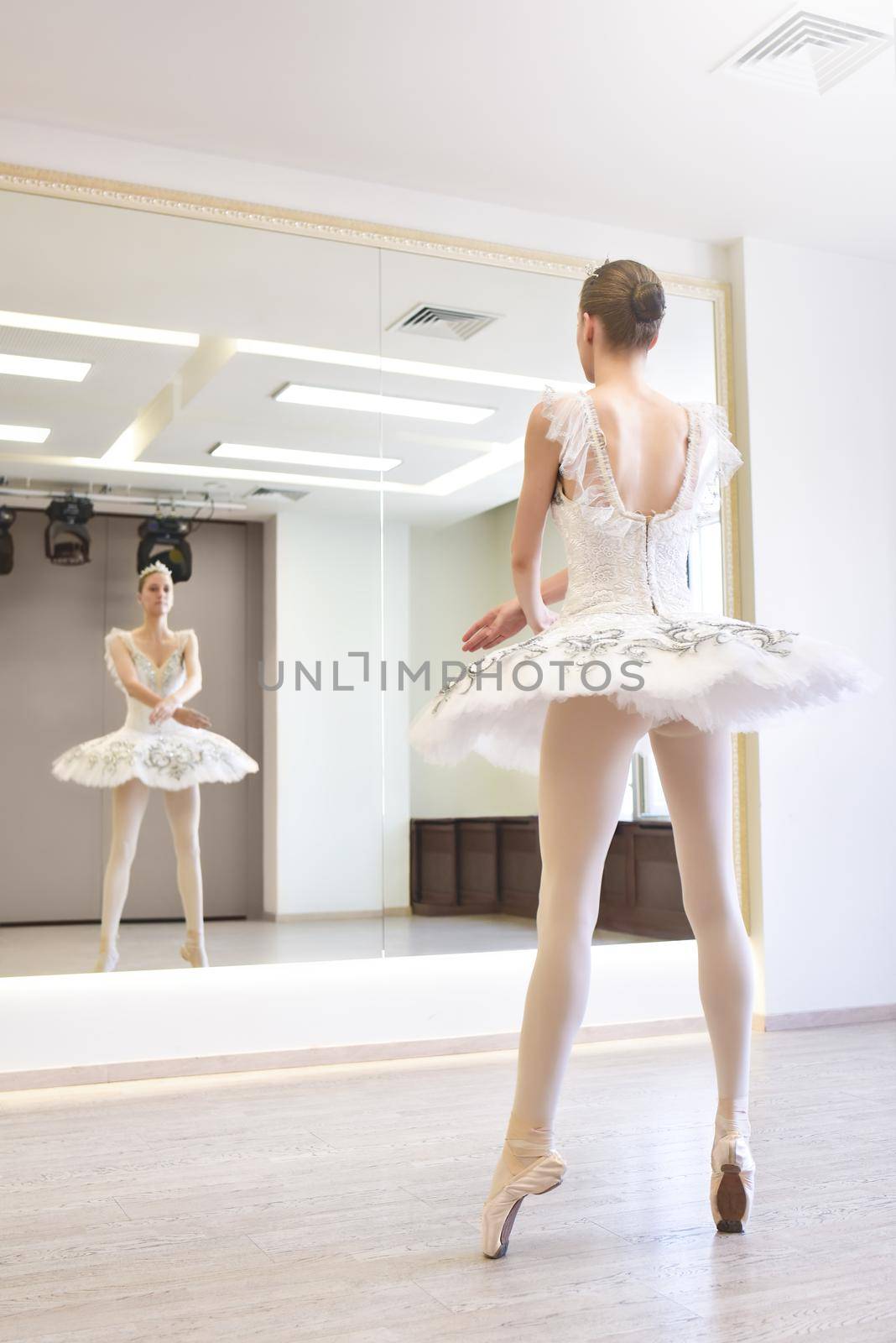 A young ballerina in a white tutu practicing in front of a mirror in the ballet studio by Nickstock