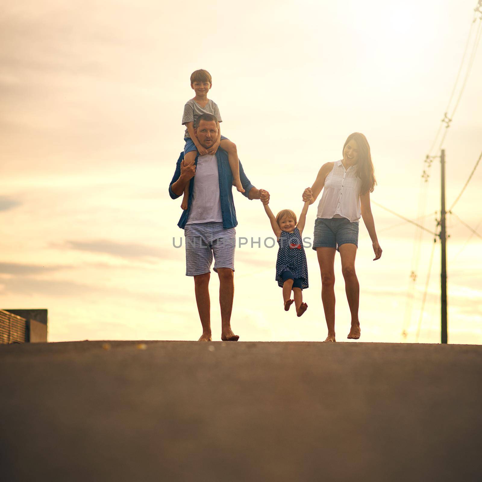 Walking through the neighbourhood as a family. a young family taking a walk down the road outside. by YuriArcurs