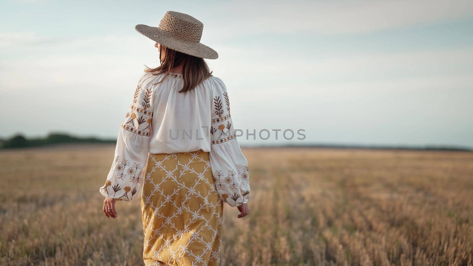 Unrecognizable ethnic woman walking in wheat field after harvesting. Attractive lady in embroidery vyshyvanka blouse and straw hat. Ukraine, independence, freedom, patriot symbol, stylish girl. photo