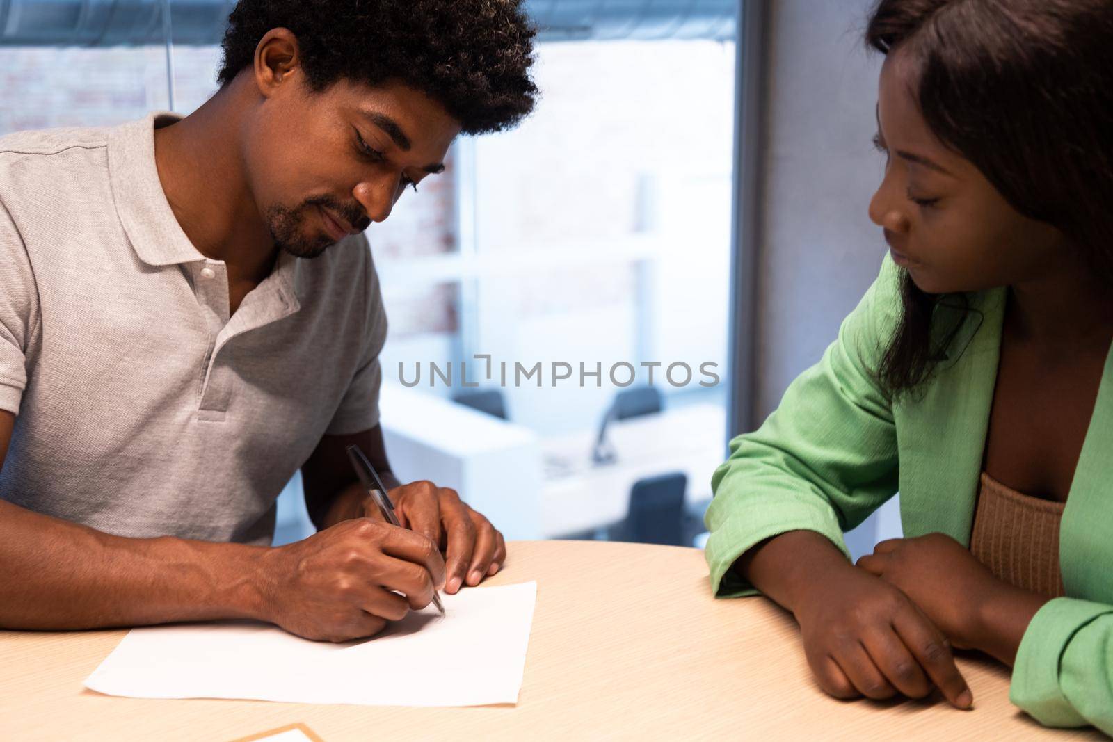 Young African American man signing agreement at business meeting. by Hoverstock