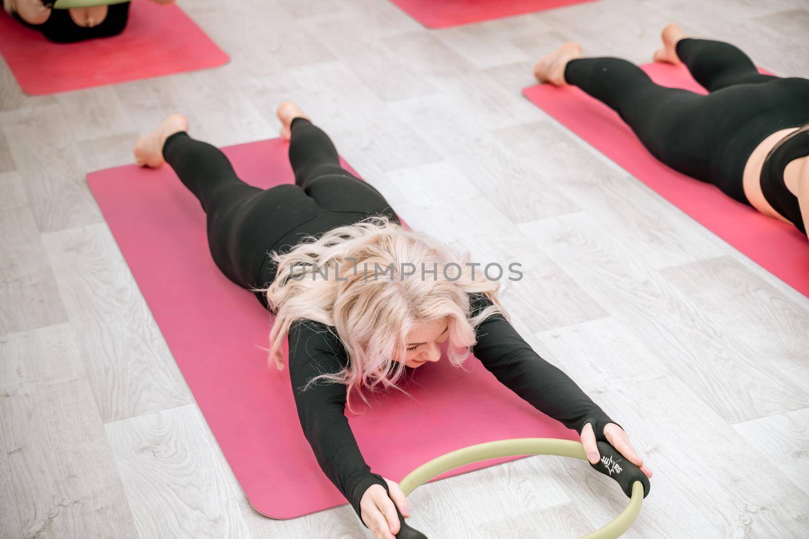 A group of six athletic women doing pilates or yoga on pink mats in front of a window in a beige loft studio interior. Teamwork, good mood and healthy lifestyle concept. by Matiunina