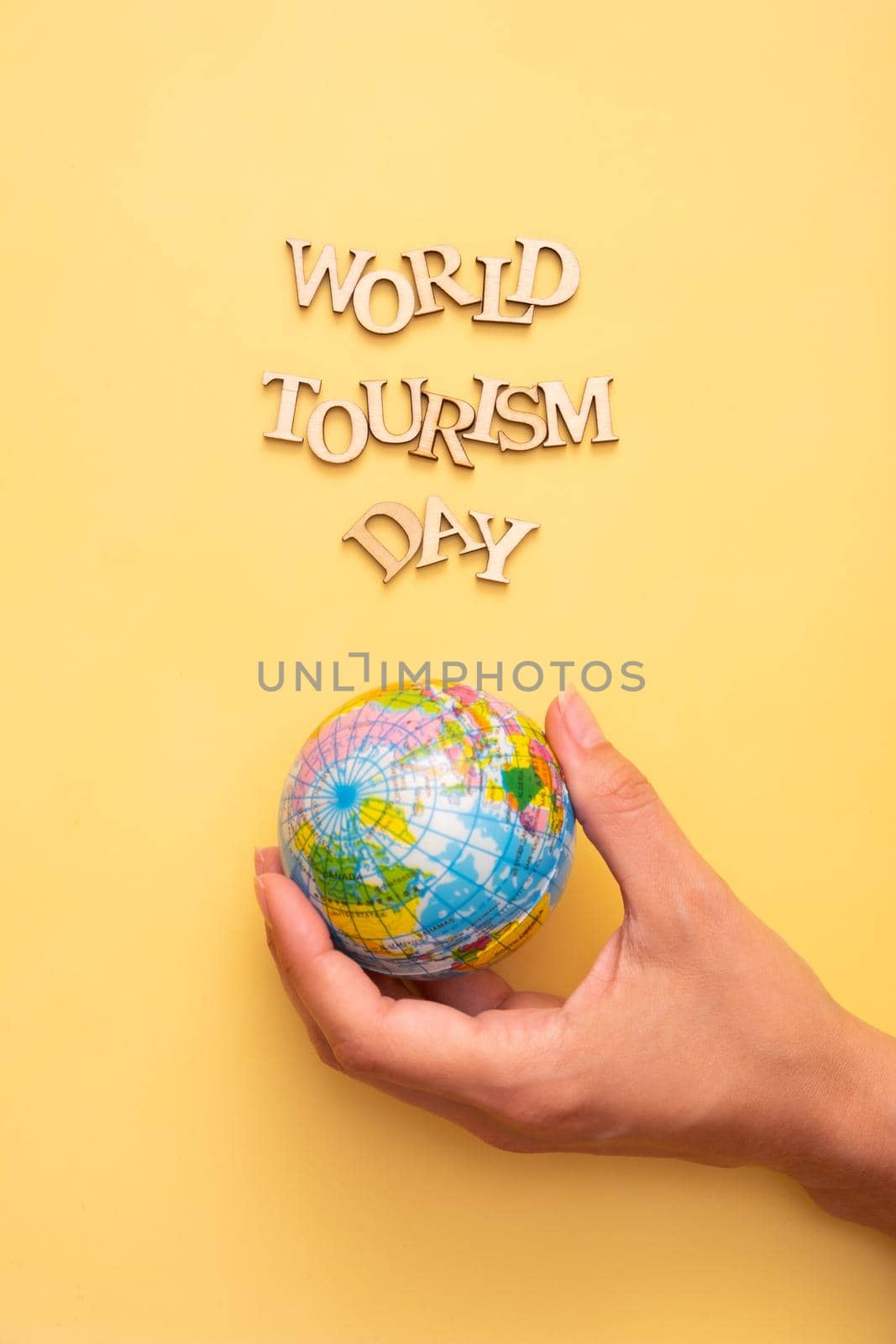 World Tourism Day text from wooden letters on a yellow color background with globe in female hands top view.