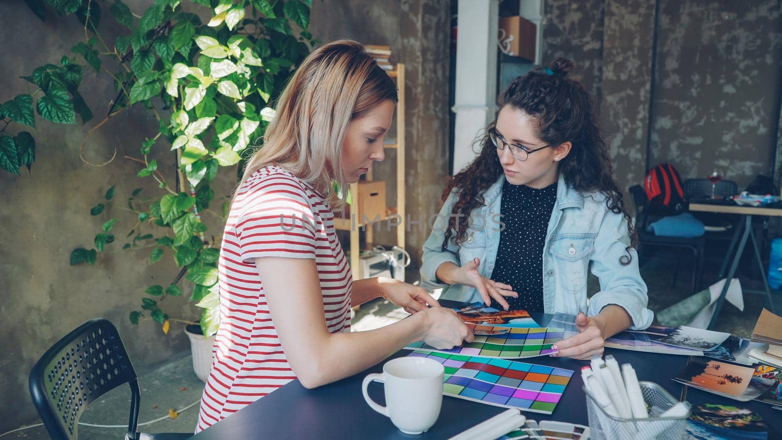 Attractive female designers are busy working with color palettes to determine colors on photograph. Work day in design company concept.